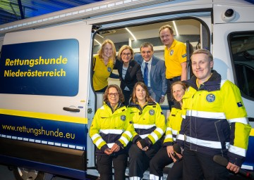 (v.l.n.r.) Geschäftsführerin Karin Kuhn, Hundeführerin Maria Raftl, Landeshauptfrau Johanna Mikl-Leitner, Hundeführerin Desiree Kerschbaumer, Obmann Anton Erber, Pressesprecher Stefan Tucek, Hundeführerin Katharina Reitl und Hundeführer Jakob Eichelter im Einsatzfahrzeug mit Namen „Anton“. Der Name des Autos erinnert an Alt-Obmann Anton Endsdorfer.